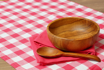Empty wooden bowl and spoon on a red checkered tablecloth.