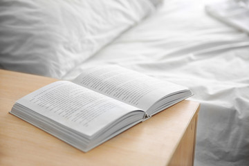 Opened book on wooden bedside table near crumpled bed