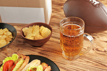 Glass of beer with snack and ball on wooden background