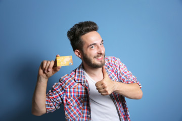 Young man holding credit card on blue background
