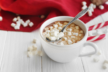 Cup of hot chocolate with marshmallows and candy on table