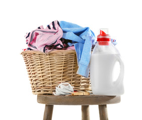 Wicker basket with baby laundry and cleanser on white background