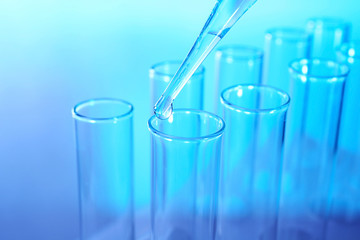 Close up of a pipette dropping a  sample into a test tube on blue background