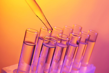 Close up of a pipette dropping a  sample into a test tube on colourful background