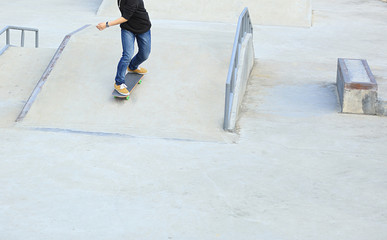 skateboarder legs riding skateboard at skatepark ramp