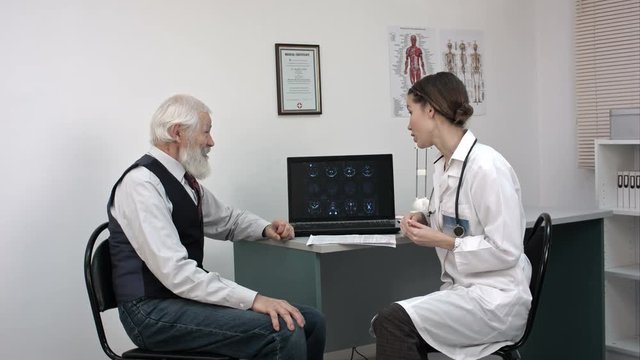 Young doctor showing mri on laptop to senior patient.