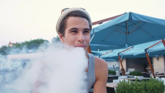 Young hipster man on fixed gear bike using advanced personal vaporizer or e-cig