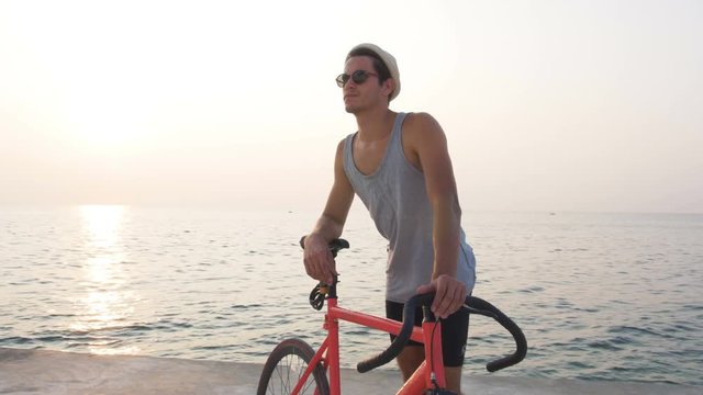 Young man with his fixed gear bike on seafront during sunset or sunrise