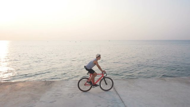 Young man riding on his fixed gear bike on seafront during sunset or sunrise