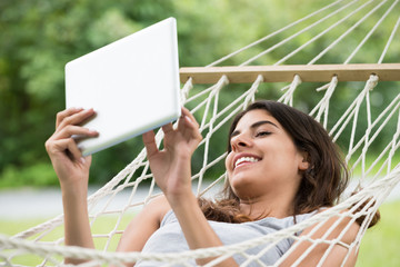 Woman Lying On Hammock Looking At Digital Tablet
