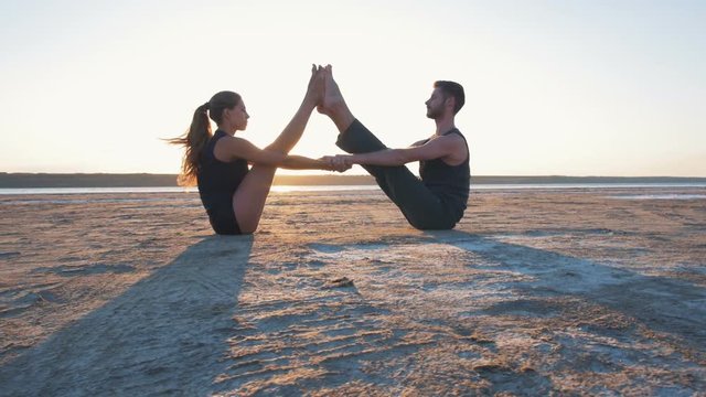 Two persons doing couple yoga nauka asana boat pose on the beach at sunset 