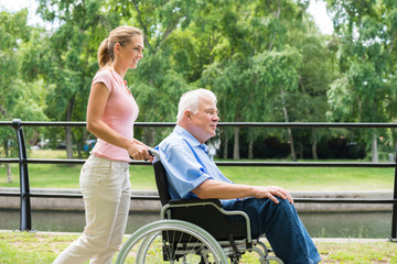 Smiling Young Woman Assisting Her Disabled Father On Wheelchair