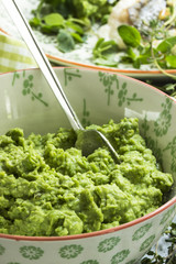 Erbsenpüree, vegan in einer Schüssel mit Löffel und einem Teller im Hintergrund