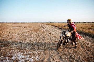 Man in golden helmet and american flag cape driving motorcycle