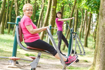 Fototapeta na wymiar Senior and young woman exercising upper and lower body on outdoor gym, healthy lifestyle