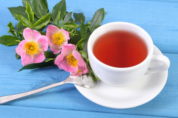 Cup of tea and wild rose flower on blue boards