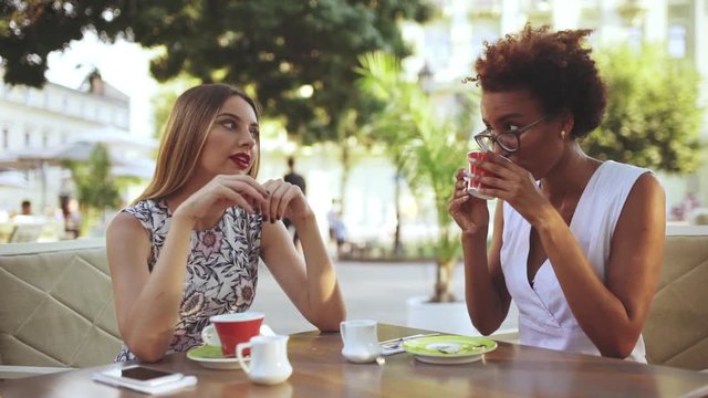 Young beautiful girls speaking, smiling, sitting in cafe. Slow motion.