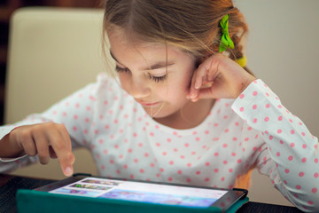 Little girl playing on her tablet at home