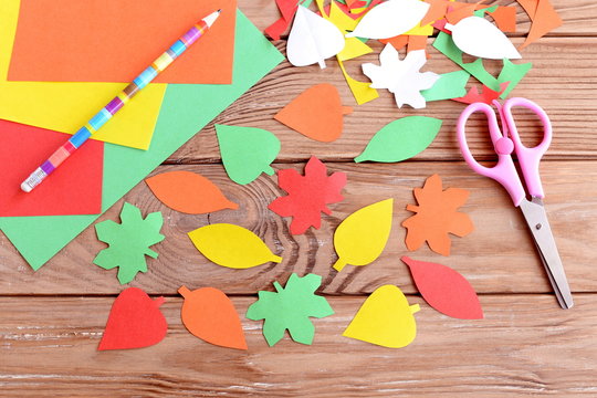 Autumn colorful leaves cut from paper, pencil, scissors, colored paper sheets on a wooden background. Teaching scissor cutting. Early learning in kindergarten and at home. Kids art