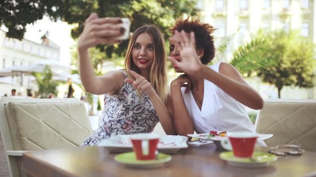 Young beautiful girls making selfie, smiling, sitting in cafe. Slow motion.