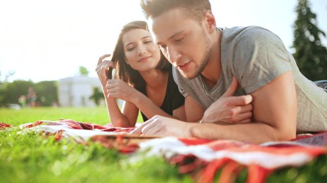 Young beautiful couple reading book, smiling, resting in park.