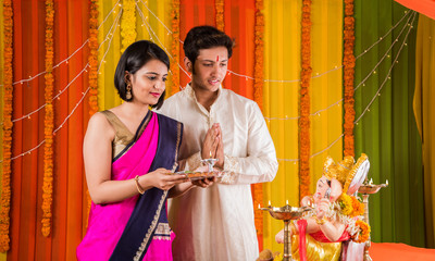 good looking Indian young couple performing puja in front of lord ganesh on ganesh festival or...