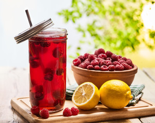 On wooden boards is ice cold drink glasses with raspberry lemon cocktail . Country ice cold drink number two hundred ninety five with raspberry clay bowl outdoor with green tree leaf.
