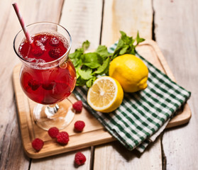 Ice cold beverage glass with raspberry lemon cocktail . Alcohol country cocktail beverage number two hundred ninety seven with raspberry on checkered napkin outdoor . Top view on wooden boards.