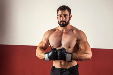 Muscular boxer in boxing gloves is looking at the camera.