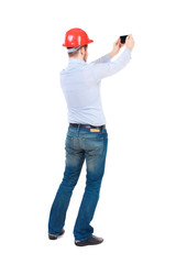 Backview of business man in construction helmet stands and enjoys tablet or using a mobile phone. Standing young guy. Rear view people collection.  backside view of person.  Isolated over white