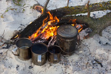 The four cups and kettle heats water on the fire. Camping  beach, summer time, fireplace