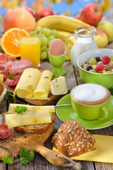 Bunter Frühstückstisch mit Käseröllchen und weiterer reichlicher Auswahl vor blauem Himmel - Outside served colorful breakfast with a large selection of food and a cup of cappuccino