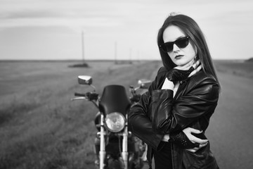 Obraz na płótnie Canvas Biker girl in a leather jacket posing near motorcycle