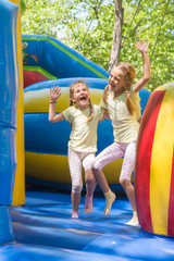Fototapeta na wymiar Two girls grimacing happily jumping on an inflatable trampoline