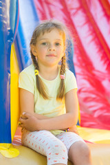 Fototapeta na wymiar Five-year girl naprygalis on a large inflatable trampoline sat down to rest