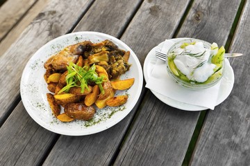 Rabbit, potato wedge and cucumber salad on wooden table