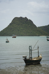 Traditional fishing  boat laying on a beach near the sea with big and long mountain in background,cloudy sky,filtered image