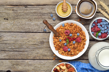 Ingredients for a healthy breakfast - berries, homemade granola, milk, dried fruits on wooden table. Copyspace background.Top view.