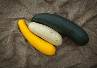 Fresh zucchini or marrow squash or courgette in basket on burlap against wooden background. Vegetables in different shapes and colors, concept of diversity