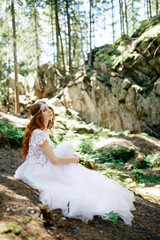 Bride with long red hair bends her back while sitting on the gro