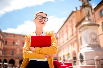 Young female student dressed casually sitting with book on the central square near university of Bologna in Bologna city in Italy. © rh2010