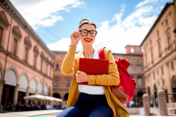 Young female student dressed casually sitting with book on the central square near university of Bologna in Bologna city in Italy. © rh2010