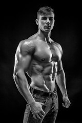 Naklejka na ściany i meble Muscular bodybuilder guy doing posing over black background