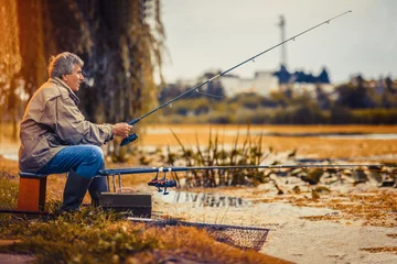 Poster Senior man fishing on a freshwater lake sitting patiently  © Mediteraneo