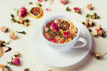 Herbal tea in white Cup and saucer with roses and dried flowers dried round slices of lemon laid on a white background