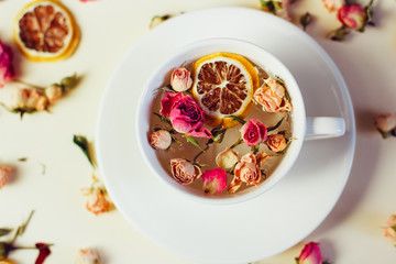 Herbal tea in white Cup and saucer with roses and dried flowers dried round slices of lemon laid on a white background