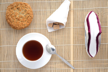 Cup of tea on a bamboo napkin, sugar, spoon, biscuits, napkins, top view