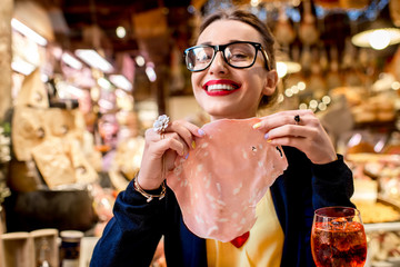 Young woman with big slice of mortadella sausage in front of food showcase in Bologna city....
