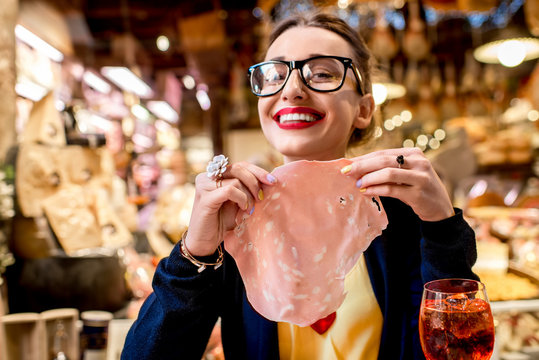 Young woman with big slice of mortadella sausage in front of food showcase in Bologna city. Mortadella was invented in Bologna city
