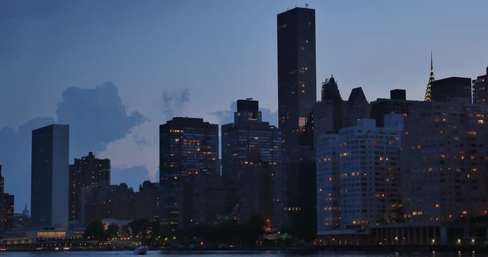 An evening or dusk establishing shot of the midtown Manhattan skyline as seen from Roosevelt Island.	 	